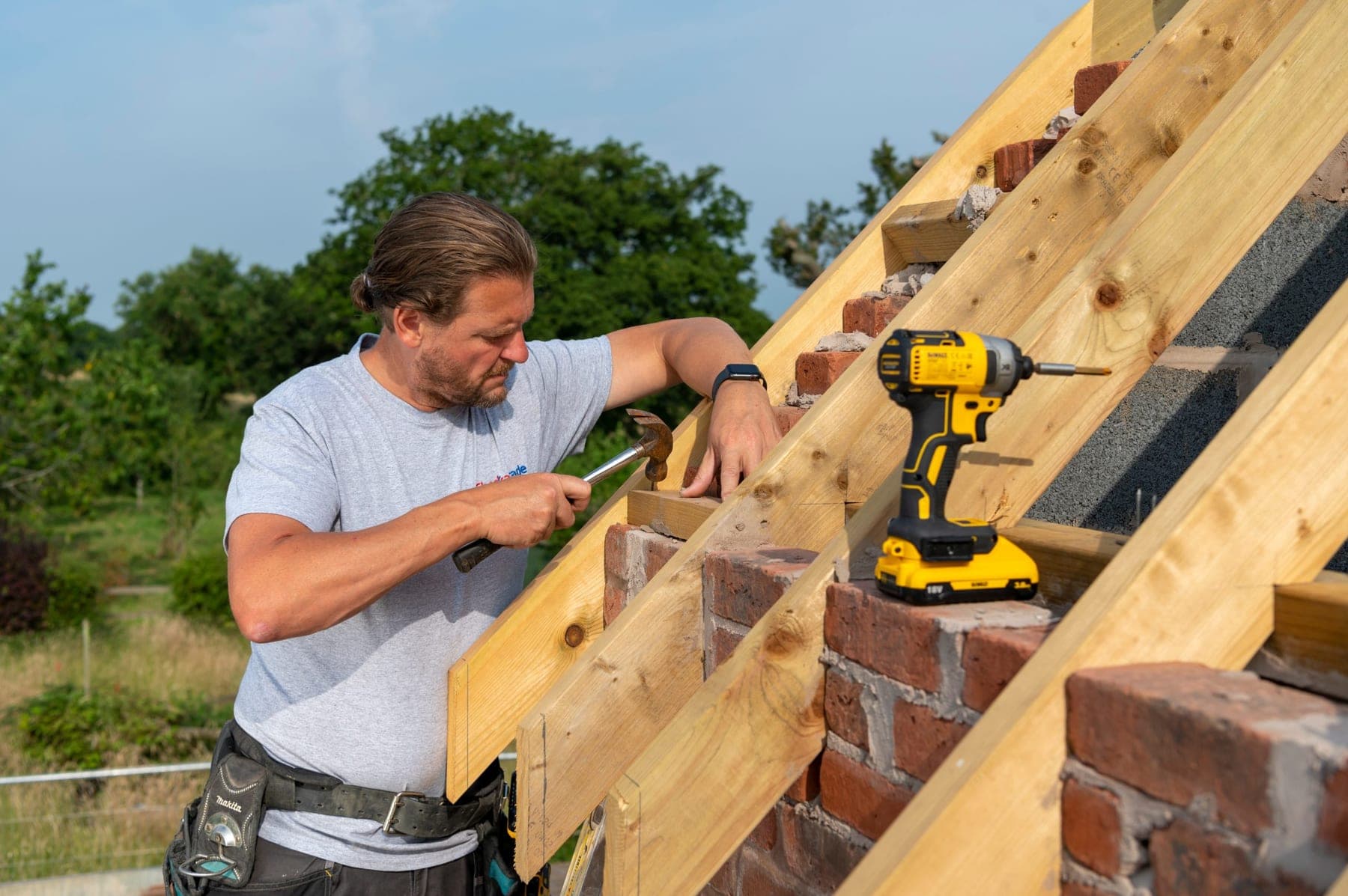 A carpenter fixing new roof timbers above a brick wall on a summer day.